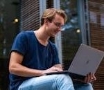 A young man sitting outdoors in Leiden, Netherlands, working on a laptop.